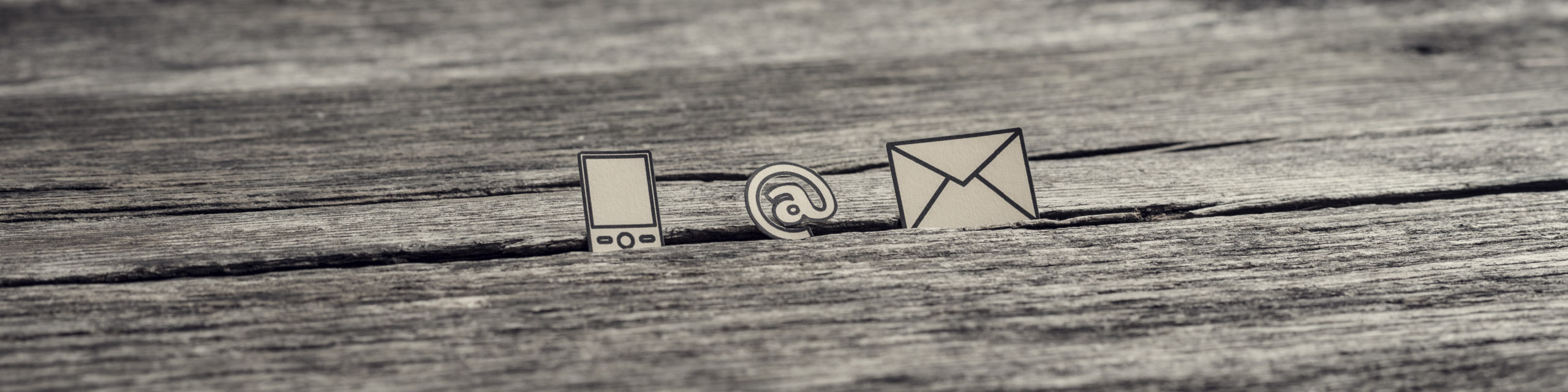 Wide panorama view of at sign, mail and mobile phone icons stuck in between a crack in the wooden surface, toned retro effect.