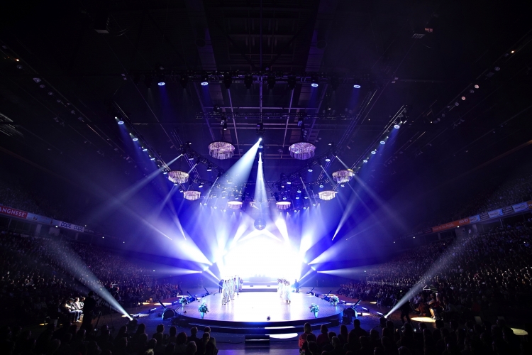 Bühne mit Lichtern und Zuschauern bei einer großen Veranstaltung in einer Arena.